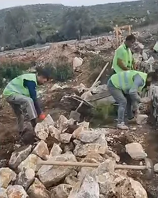 İki işçi yamaçta büyük taşları istinat duvarı için dizerken, önlerinde taş yığını ve kazılmış toprak