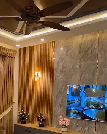 Oturma odasında ahşap çıtalı ve mermer desenli duvar, duvar aplikleri, gri TV ünitesi ve tavan pervanesi
