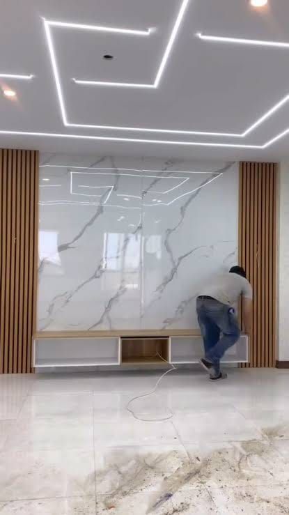 Işık hatlı beyaz tavan, damarlı mermer duvar, iki yanında ahşap çıtalar ve duvarda çalışan usta